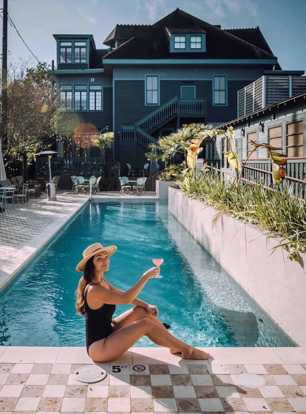 Woman posing by a residential swimming pool in a black one-piece bathing suit.
