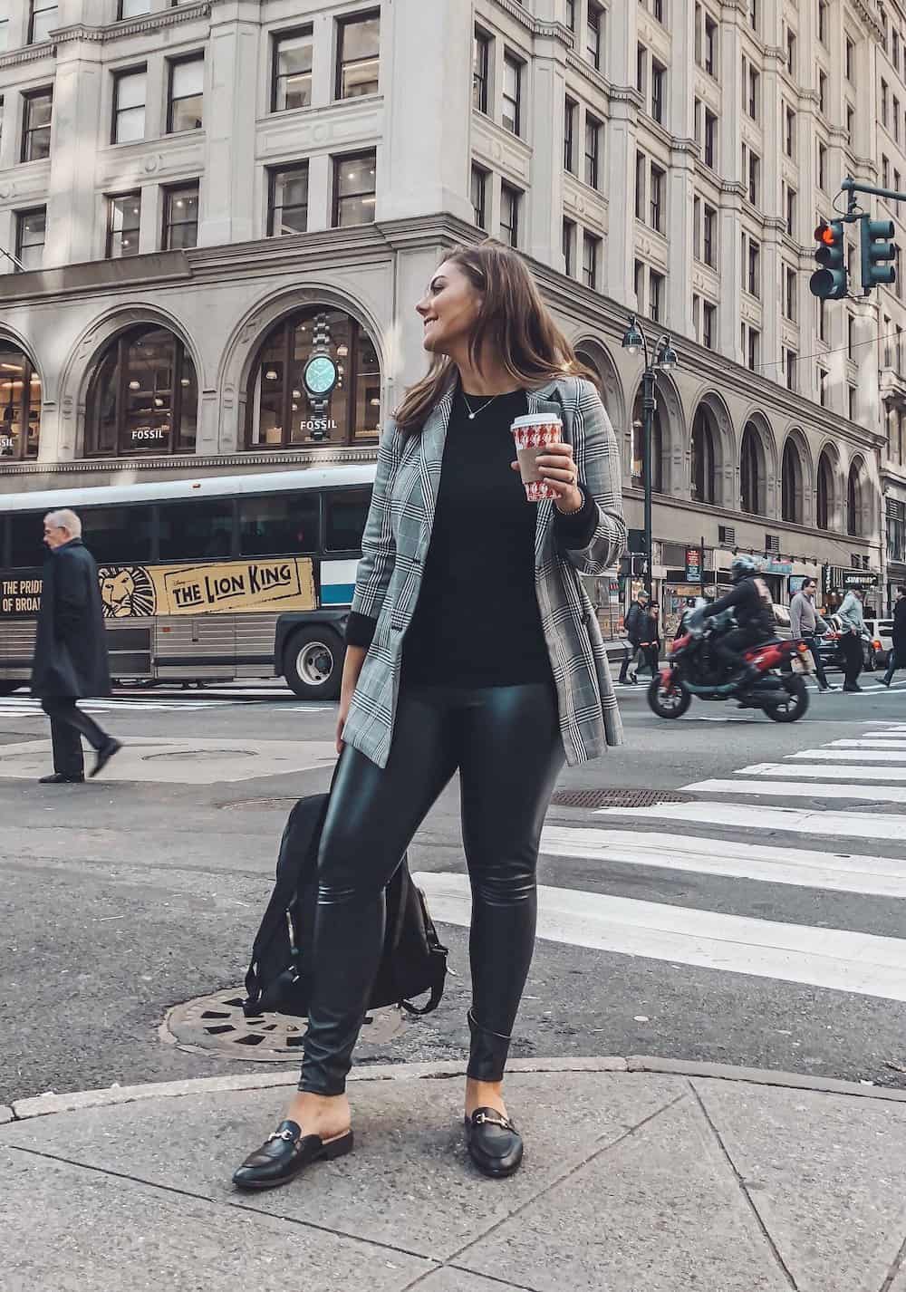 image of a woman on a busy street wearing a plaid blazer, faux leather leggings, and black loafers