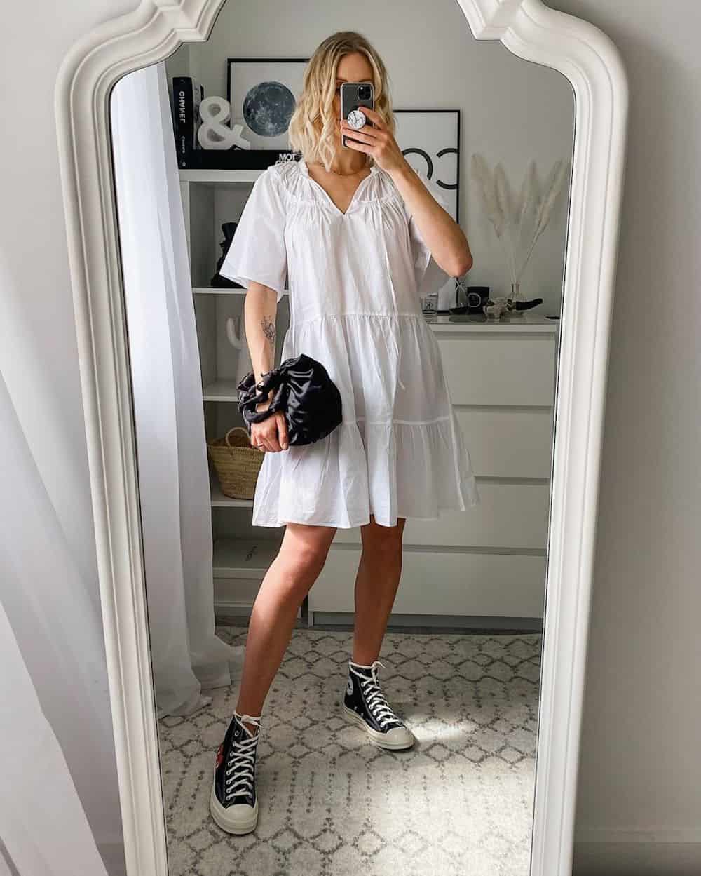 image of a woman in a white cotton tiered mini dress with puff sleeves and black converse sneakers