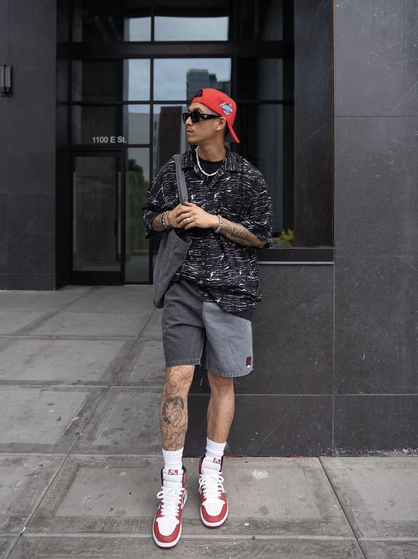 image of a man wearing a grey sweater and shorts, and red and white sneakers, with a red cap