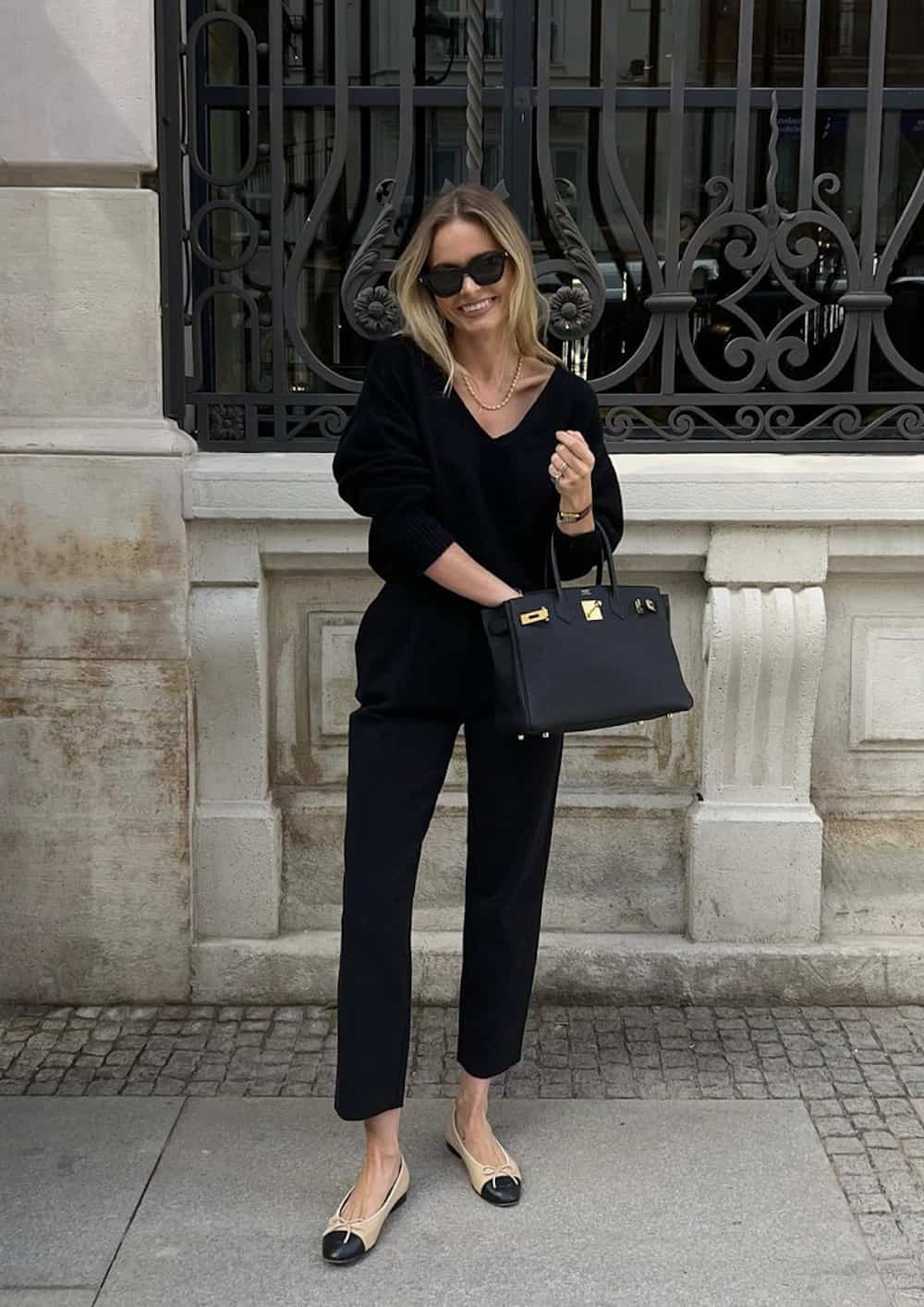 image of a woman wearing a black sweater and black pants holding a small black Hermes Birkin bag