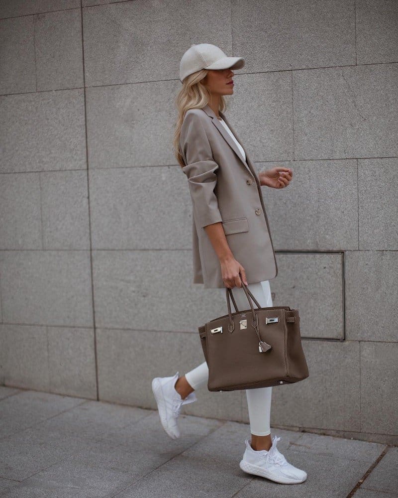 image of a blonde woman walking wearing a beige blazer and white jeans with a brown Hermes Birkin bag