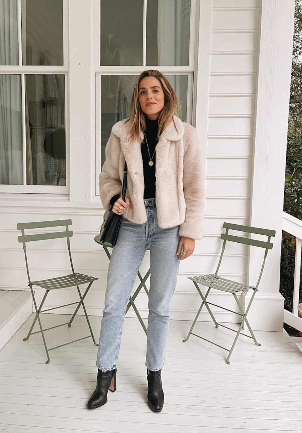 Woman wearing jeans, black booties, a black sweater and a white faux fur jacket.