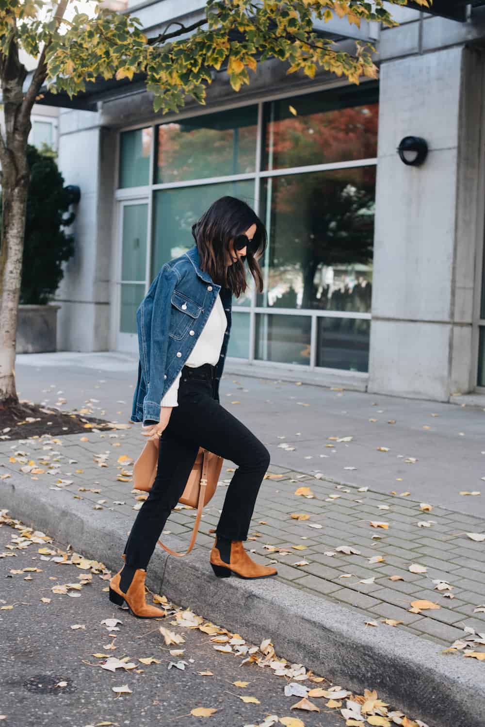 Woman wearing black jeans, brown booties, a white sweater and a denim jacket.