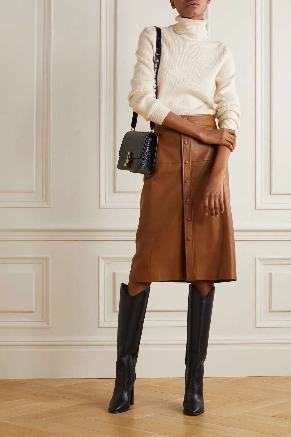 Woman wearing a leather skirt, black boots and a white turtleneck sweater.