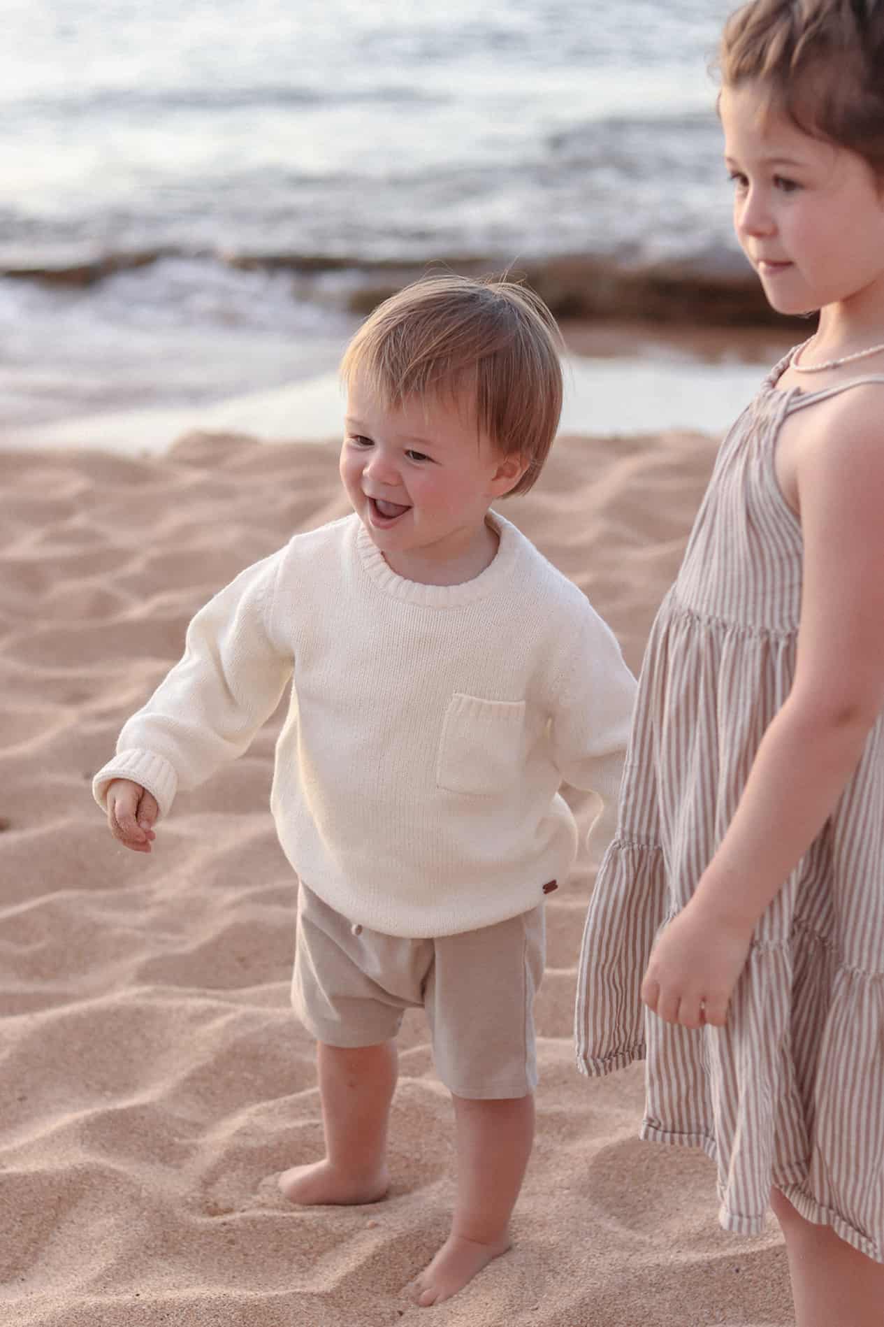 image of a small toddler boy at the beach wearing an ivory knit sweater and beige shorts