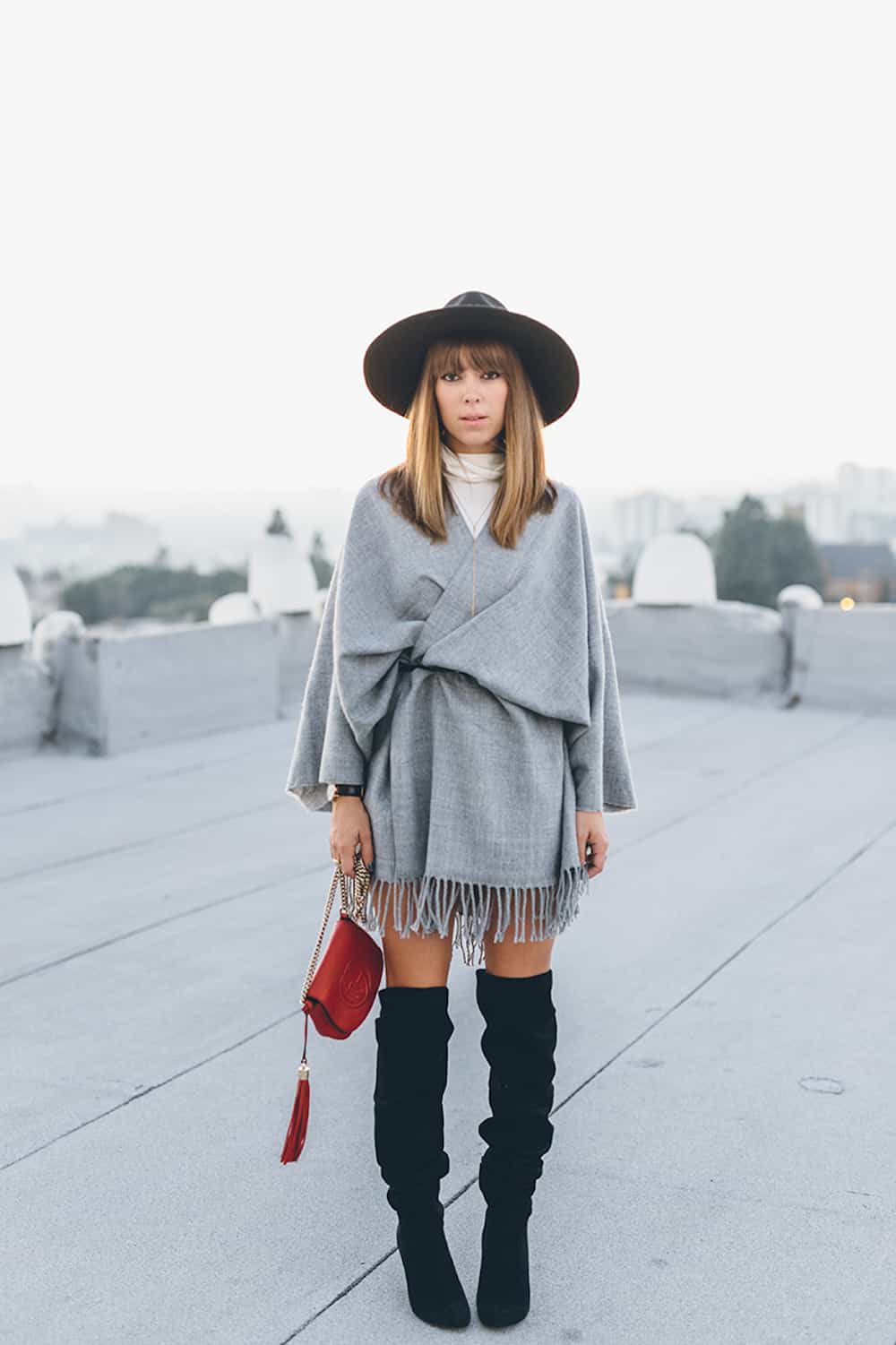 image of a woman in a grey poncho with a belt around the waist and black over the knee suede boots