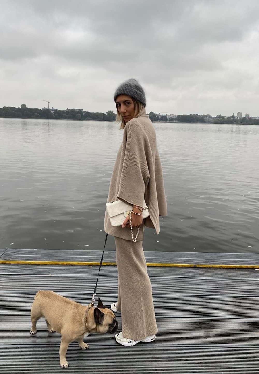 image of a woman in a matching beige knit poncho and pant set standing on a dock with a small dog