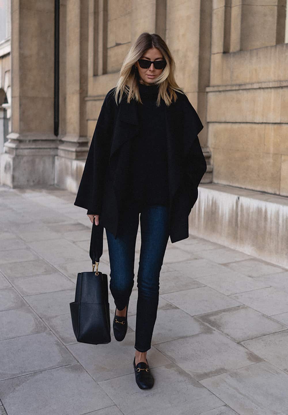 image of a woman in a black poncho, dark blue jeans, and black loafers