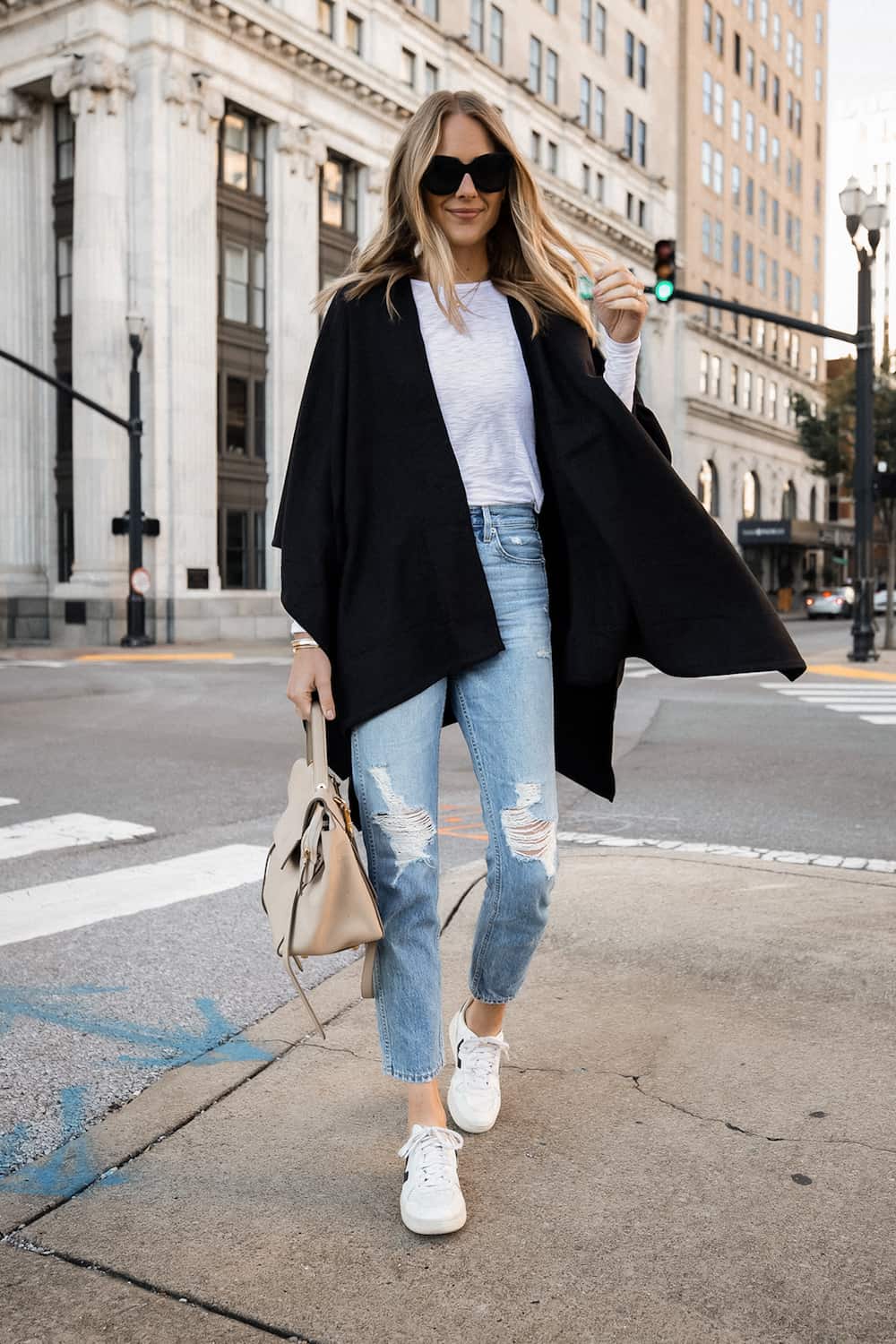image of a woman wearing an open black poncho, white top, blue jeans, and white sneakers