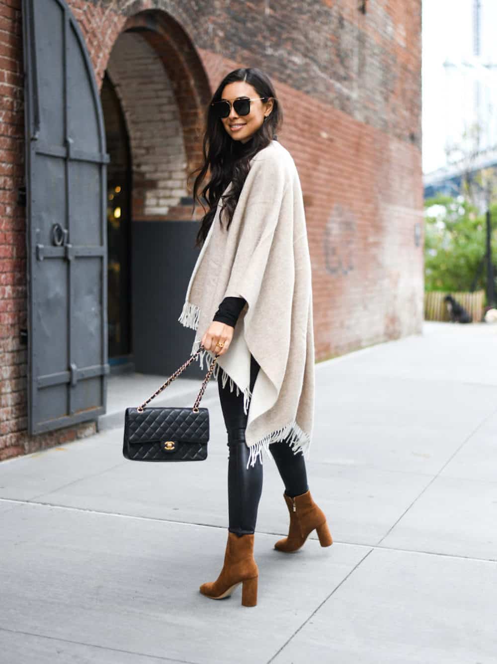 image of a woman in a beige poncho with fringe, black leather leggings, and brown suede ankle boots