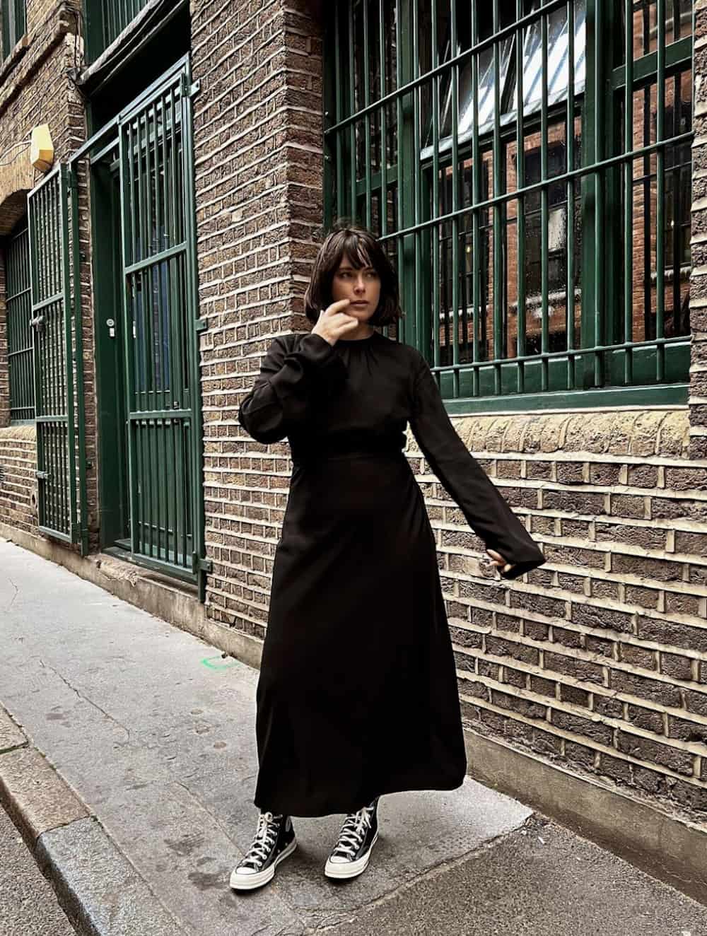 Woman wearing a black dress and sneakers.