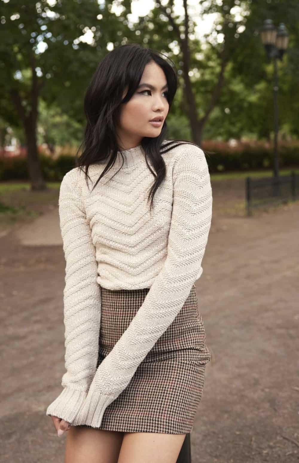 Woman wearing a white sweater and a plaid skirt.