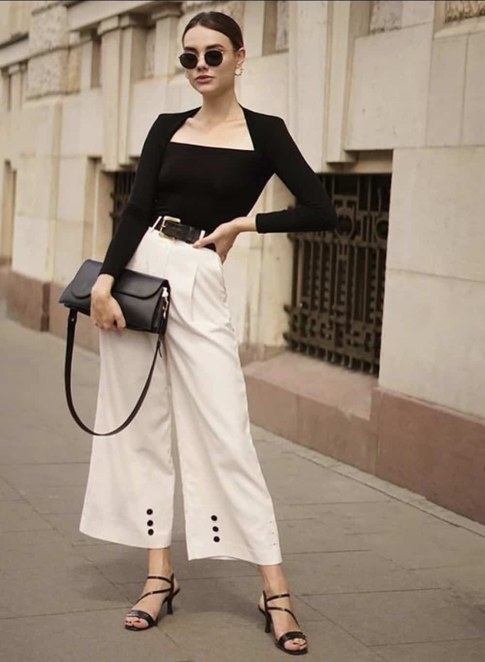 Woman wearing white, wide leg pants and a black sweater.