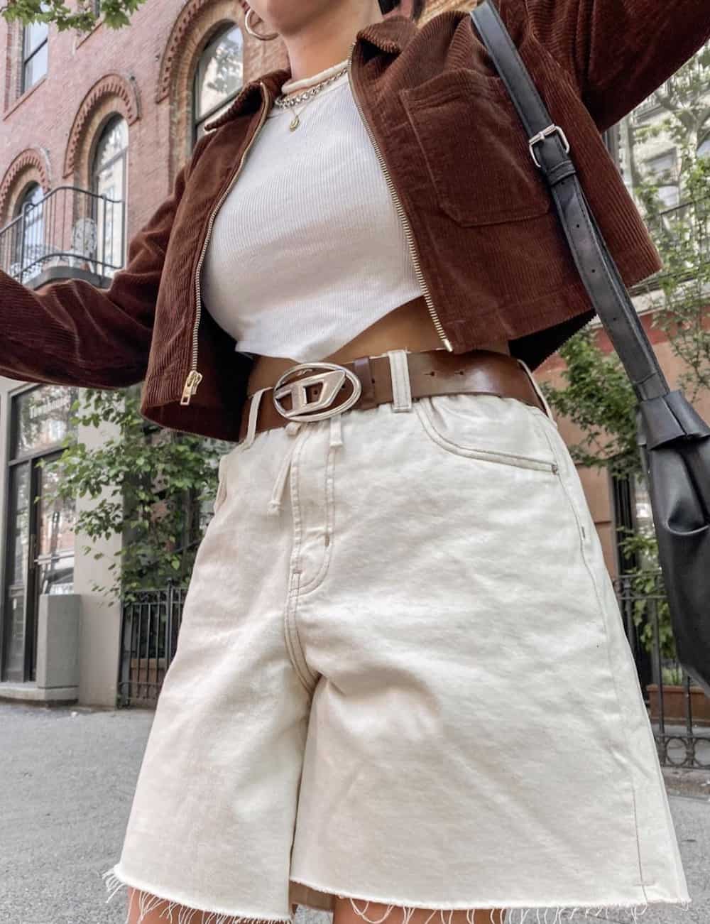 Woman wearing white denim shorts, a white crop top and a brown cropped jacket.