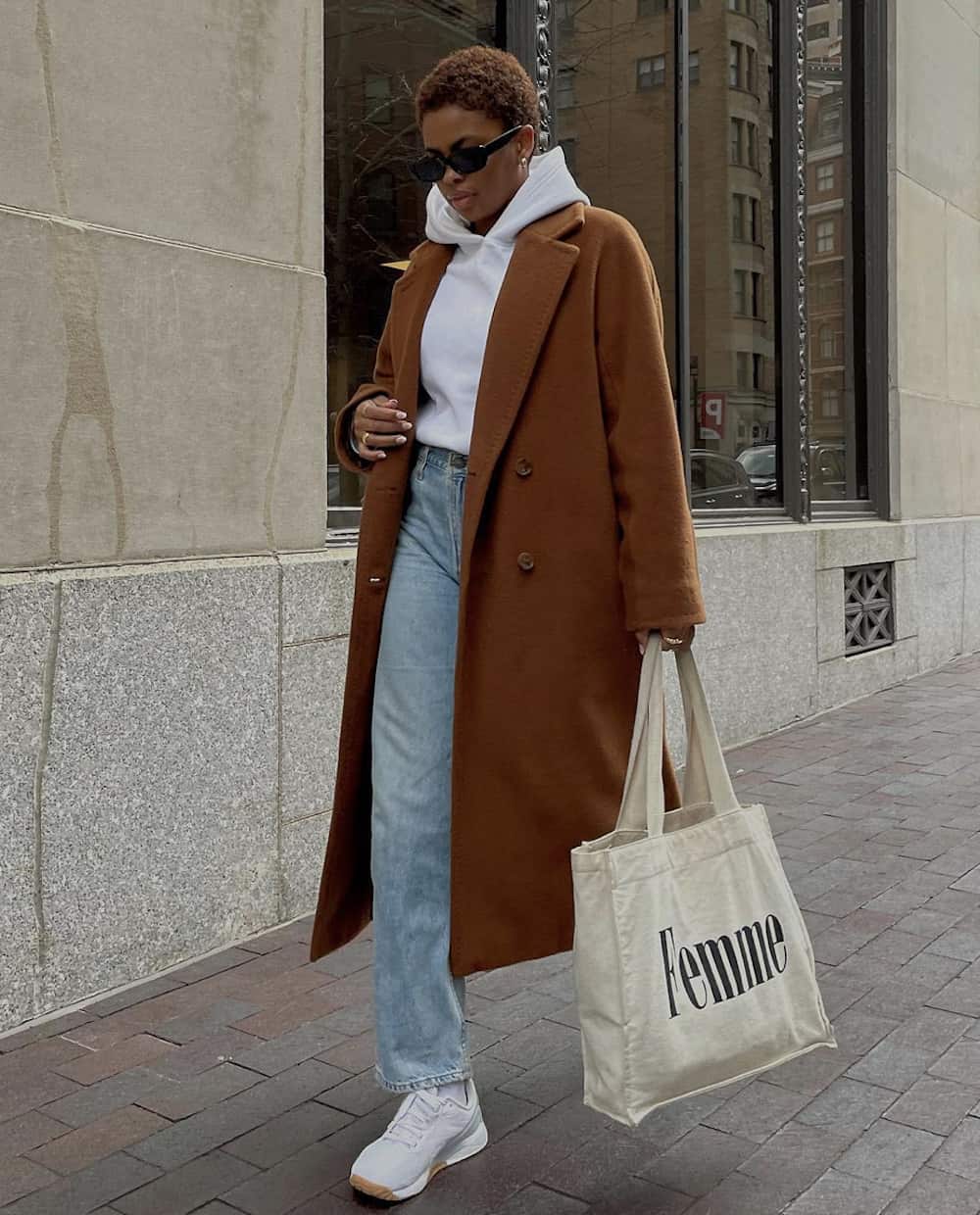 image of a stylish black woman in a long camel coat, white hoodie, jeans, and sneakers