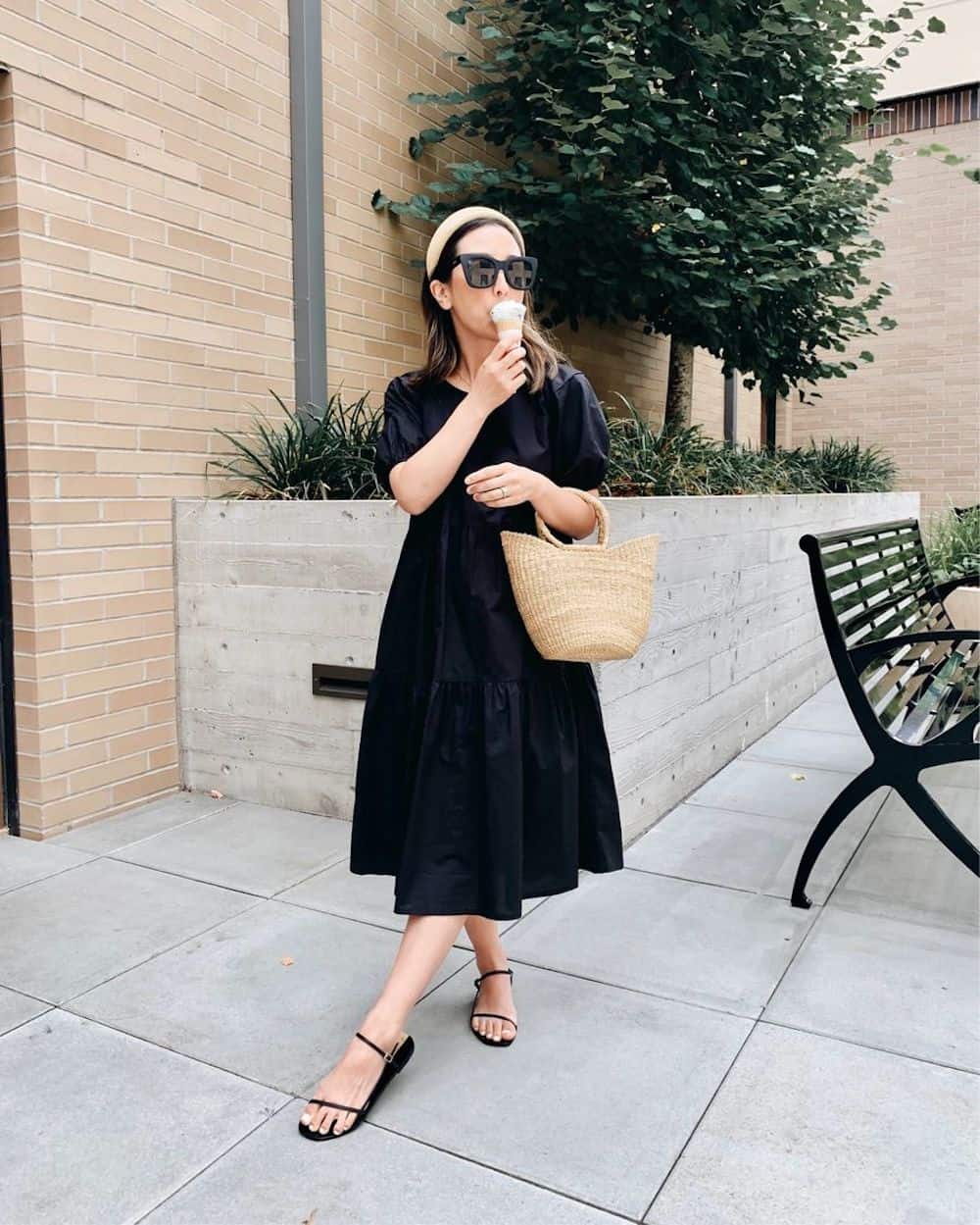 image of a woman eating an ice cream wearing a black midi dress, black sandals, and a raffia bag