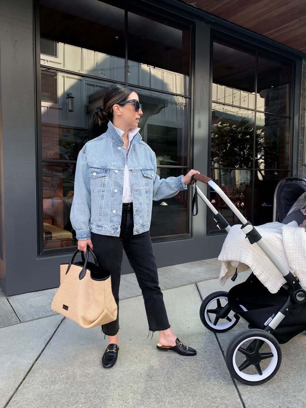 image of a woman pushing a stroller wearing black jeans, a white top, a denim jacket, and black mules