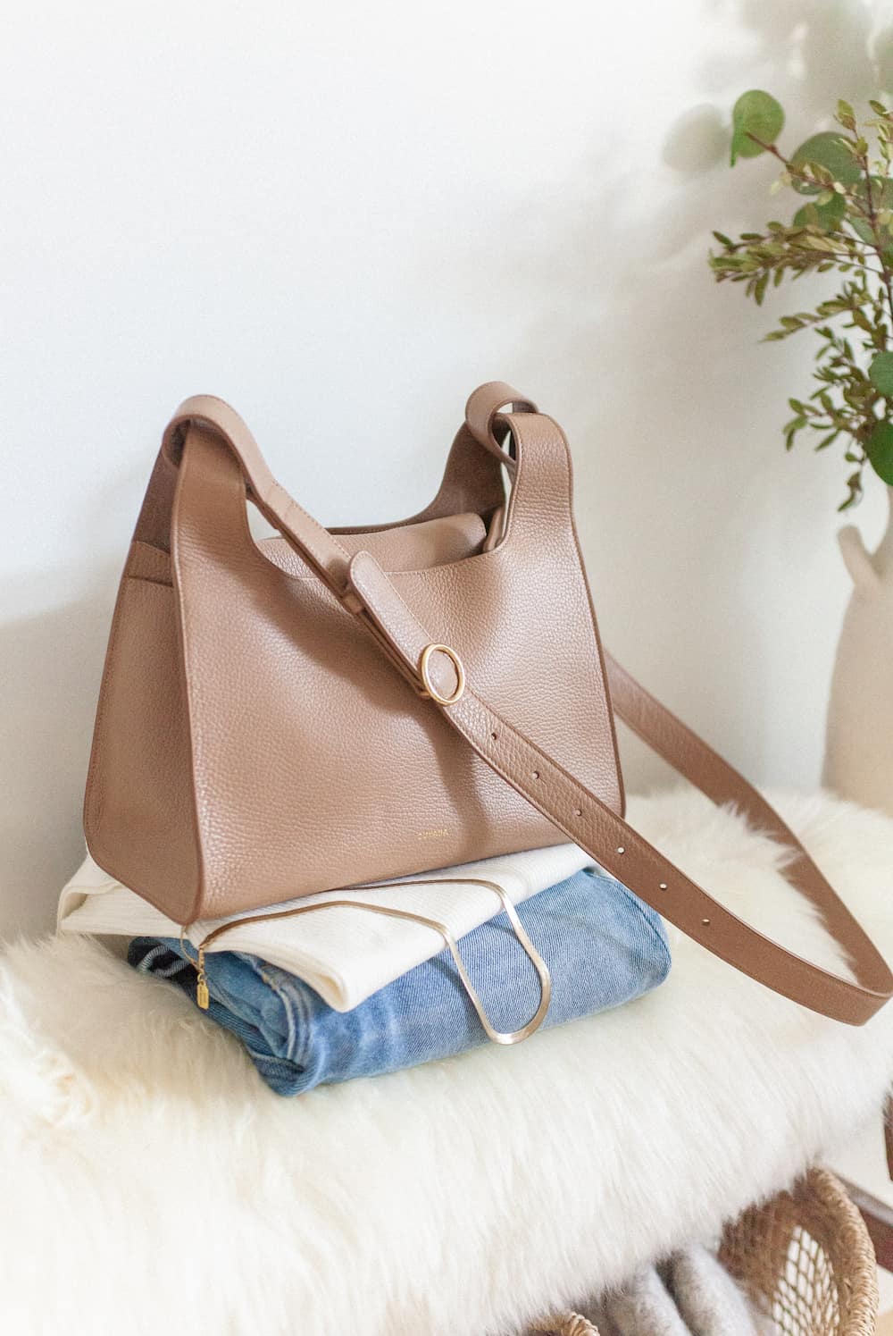 image of a Cuyana double loop bag sitting on top of a folded white tank top and blue jeans on a bench