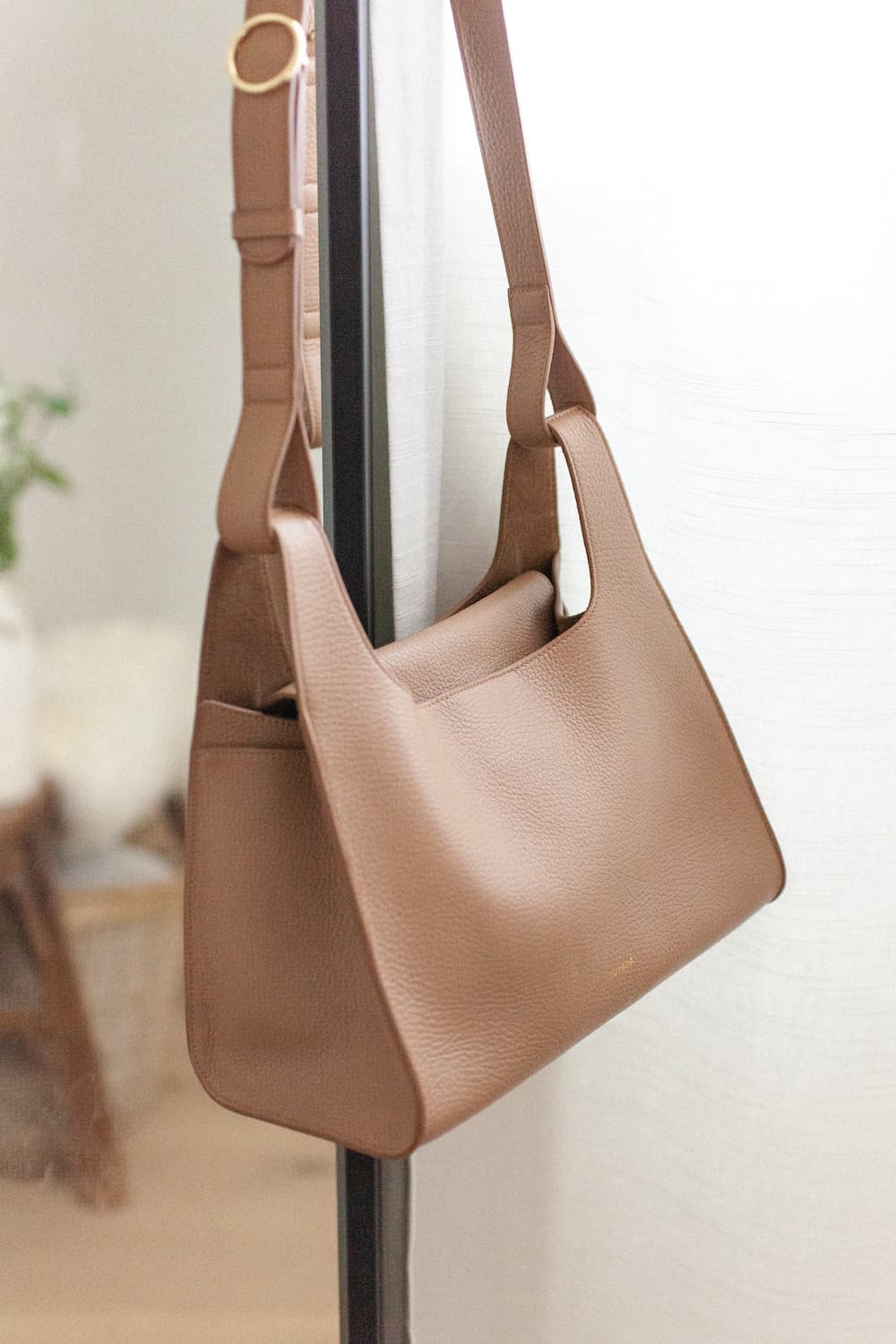 image of a brown leather Cuyana double loop bag hanging on a black framed mirror