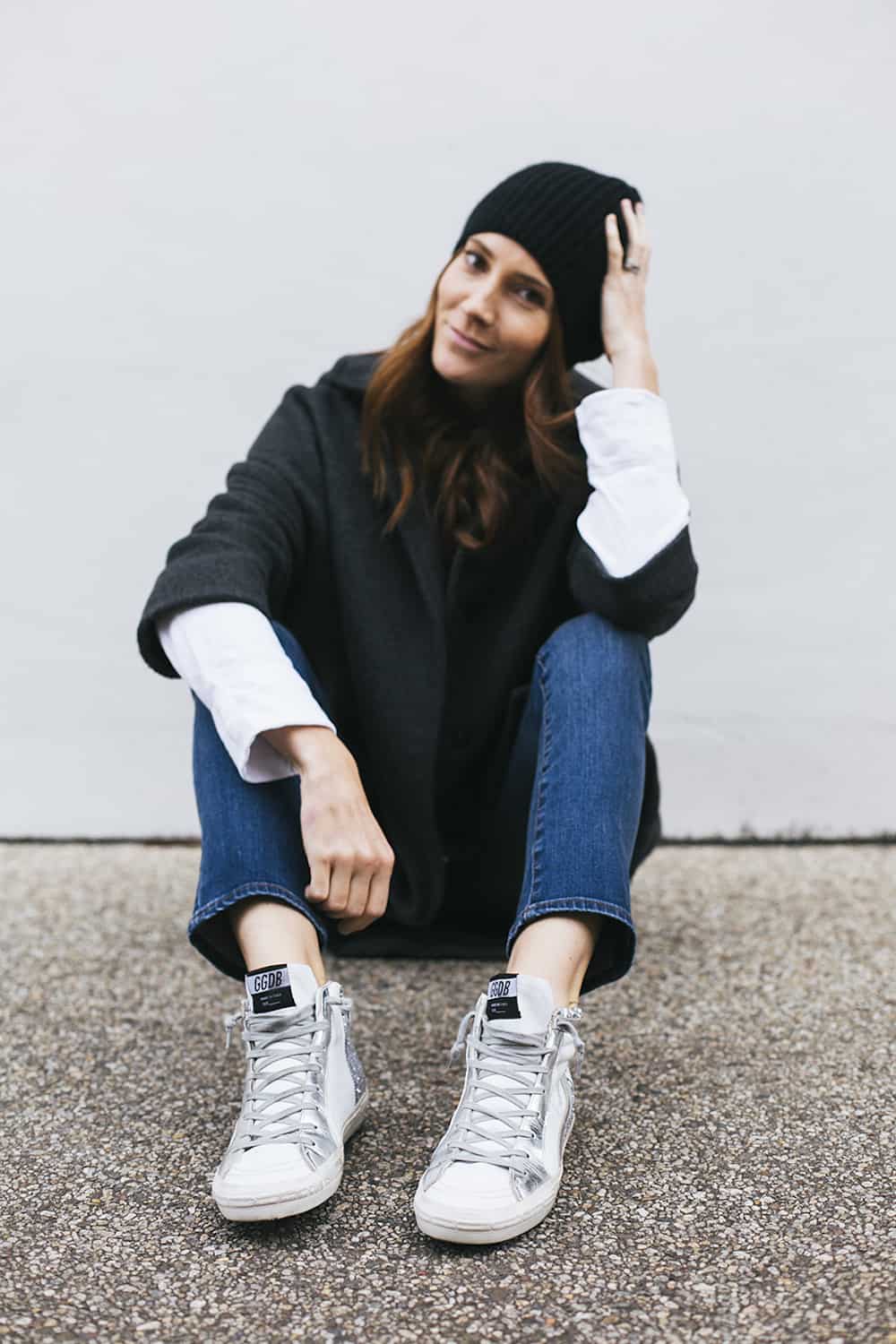 image of a woman wearing a black toque, dark sweater, jeans, and high top sneakers with a star design
