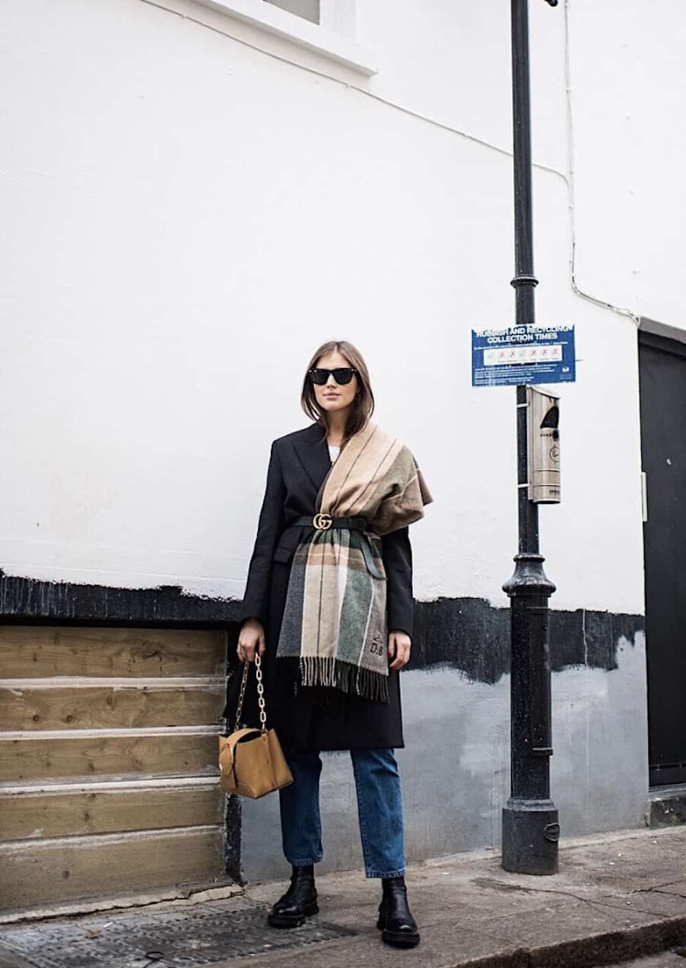image of a woman wearing a long wool coat with a large scarf tucked into a Gucci belt at the waist, jeans, and boots