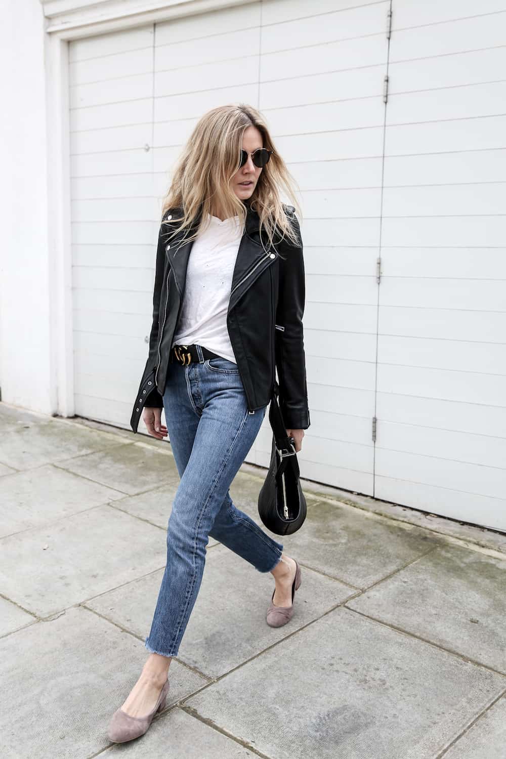 image of a woman wearing a leather jacket, white t-shirt, black Gucci belt, and blue jeans, with taupe pumps