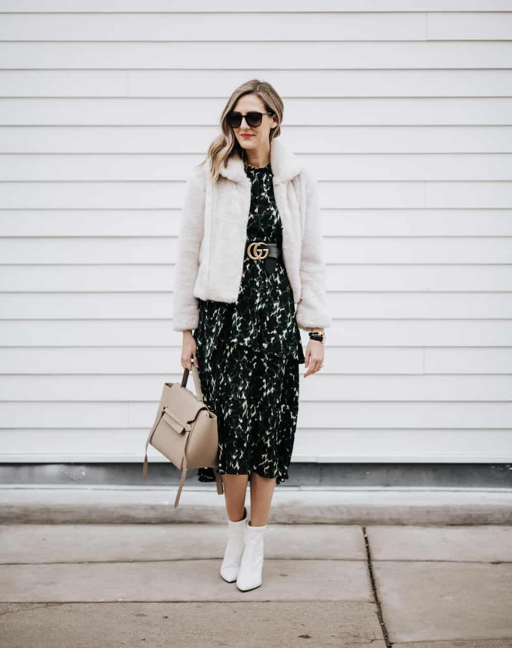 image of a woman wearing a black floral midi dress with a Gucci belt over top, a faux fur cropped jacket and white leather ankle boots