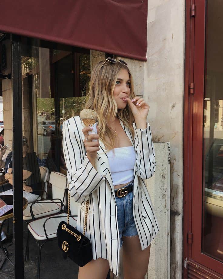 image of a young woman wearing a striped blazer, white crop top, and denim shorts with a black Gucci belt