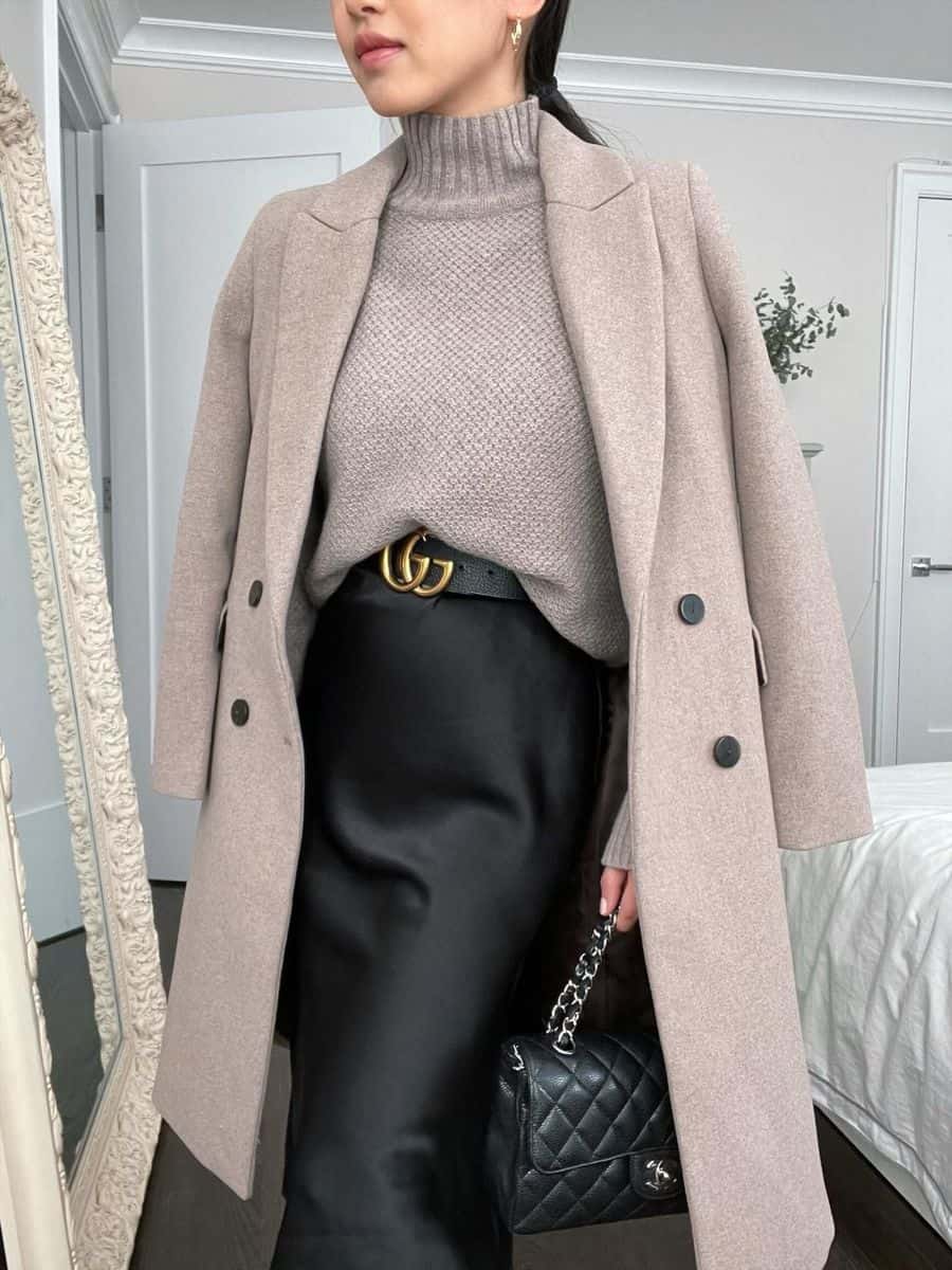 image of a woman wearing a black slip dress with a taupe sweater and a black Gucci belt, along with a wool coat draped over her shoulders