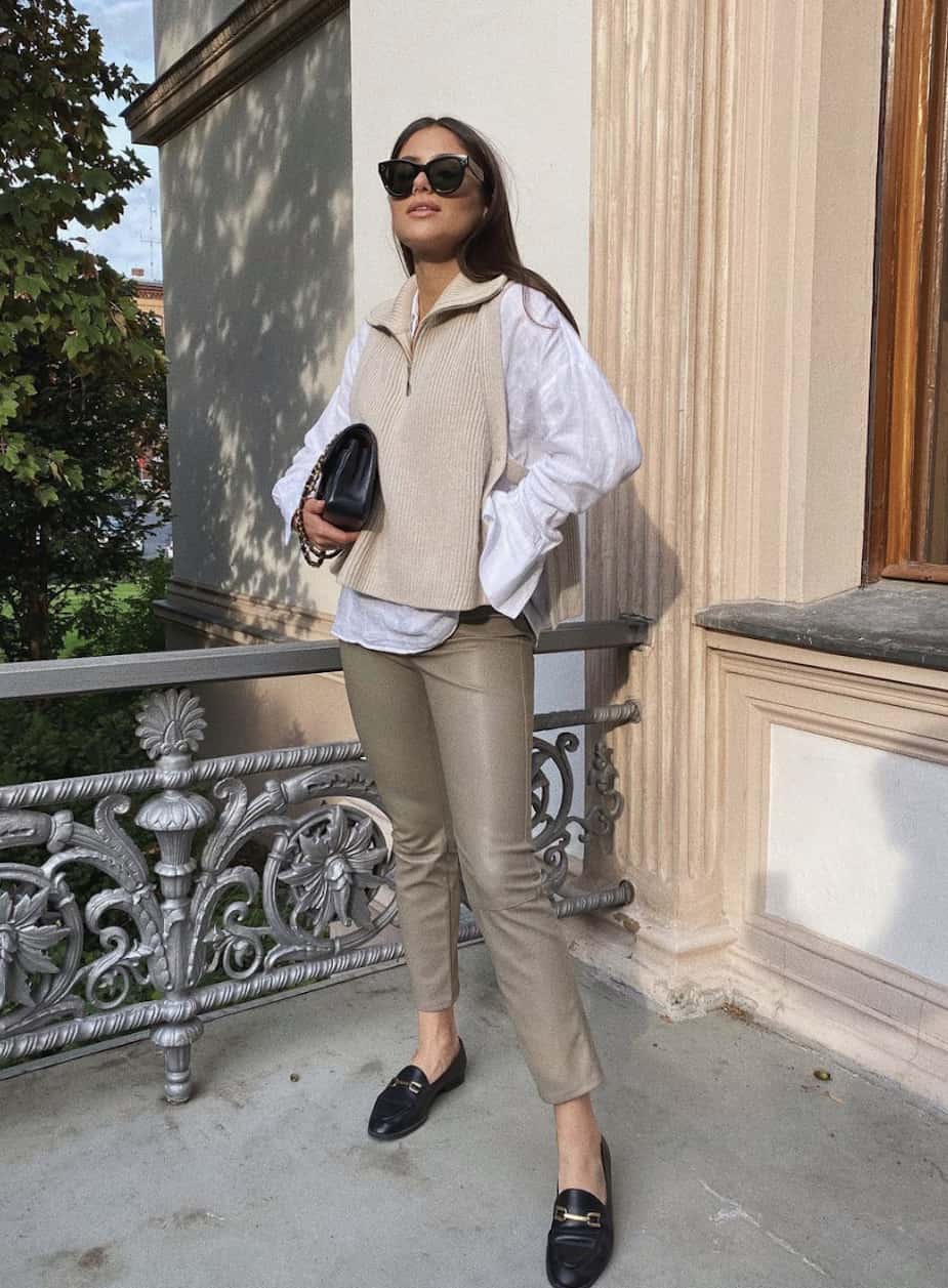 image of a woman wearing a white blouse with beige sweater vest, neutral leather leggings, and black loafers