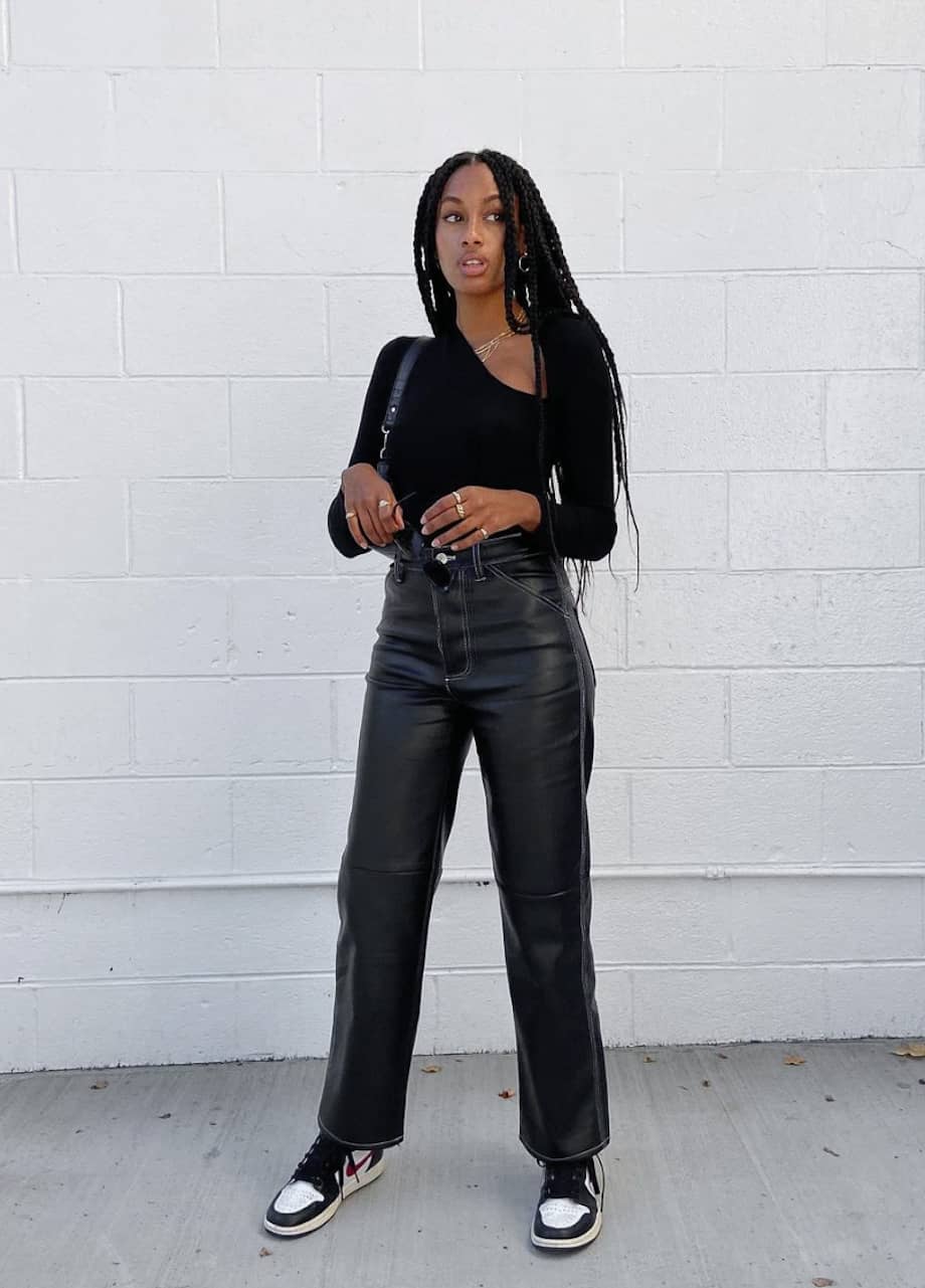 image of a chic black woman wearing a black long sleeve shirt and leather pants with sneakers