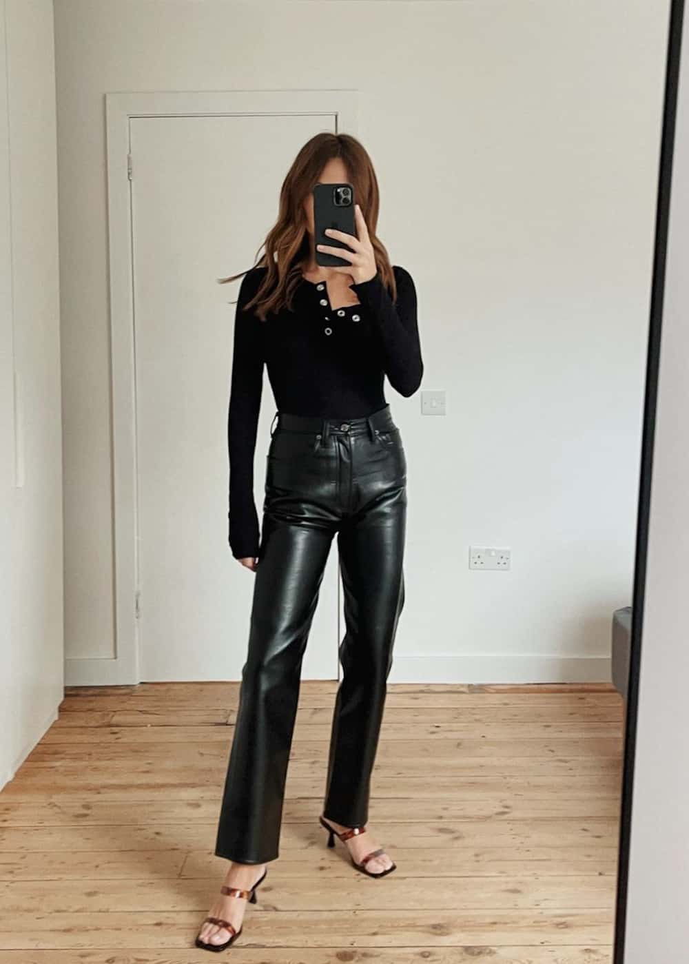 image of a woman in a long sleeve black henley shirt and long straight leg black leather pants with heeled sandals