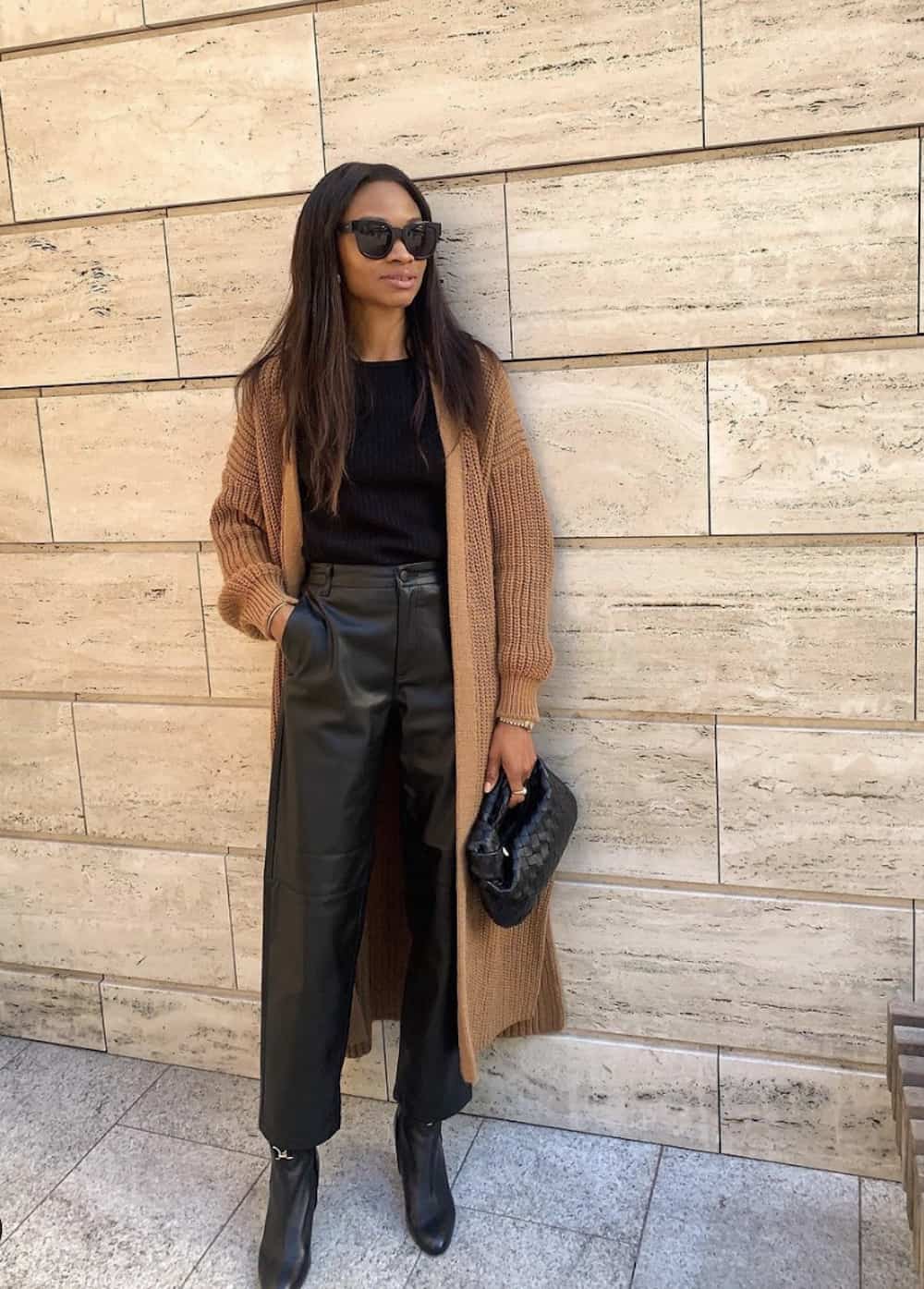 image of a black woman wearing a long camel cardigan, black top, black leather trousers, and black ankle boots