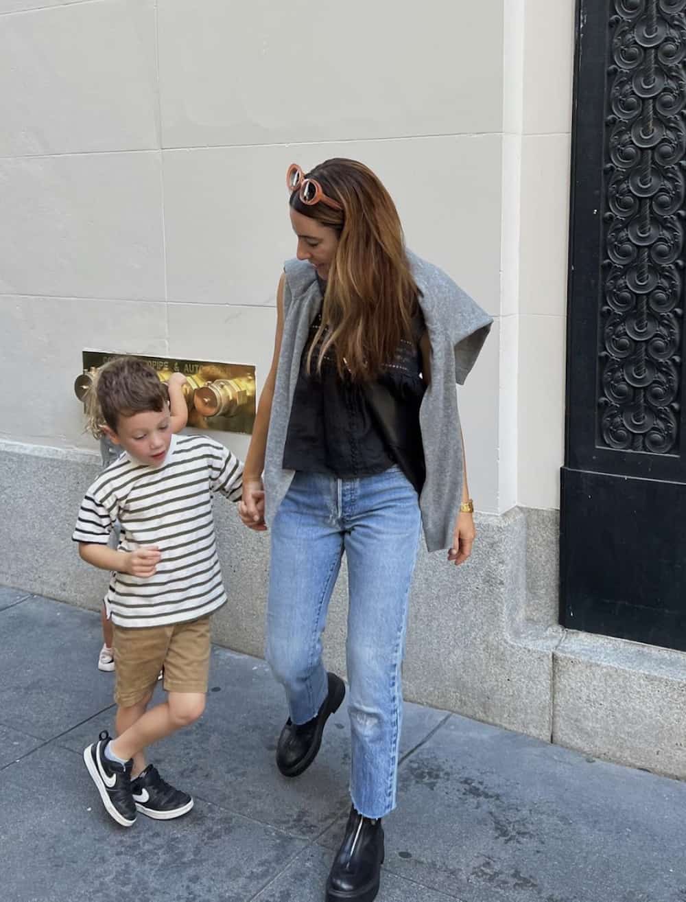 image of a woman wearing jeans, a black tank, grey sweater, and black boots with her son