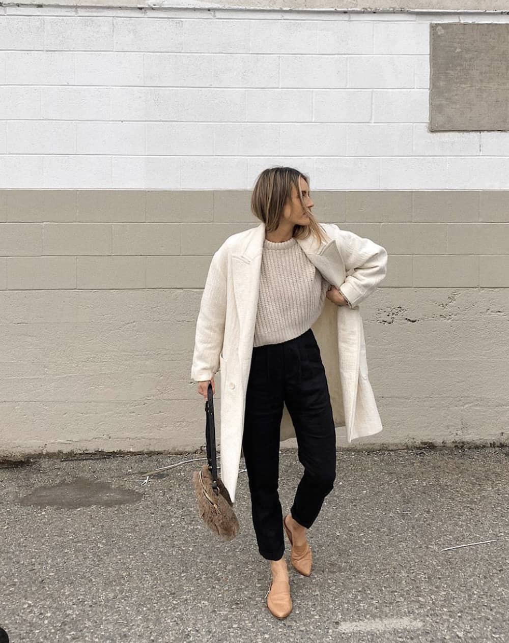 image of a woman in a cute mom outfit wearing a beige coat, knit sweater, black jeans, and brown loafers