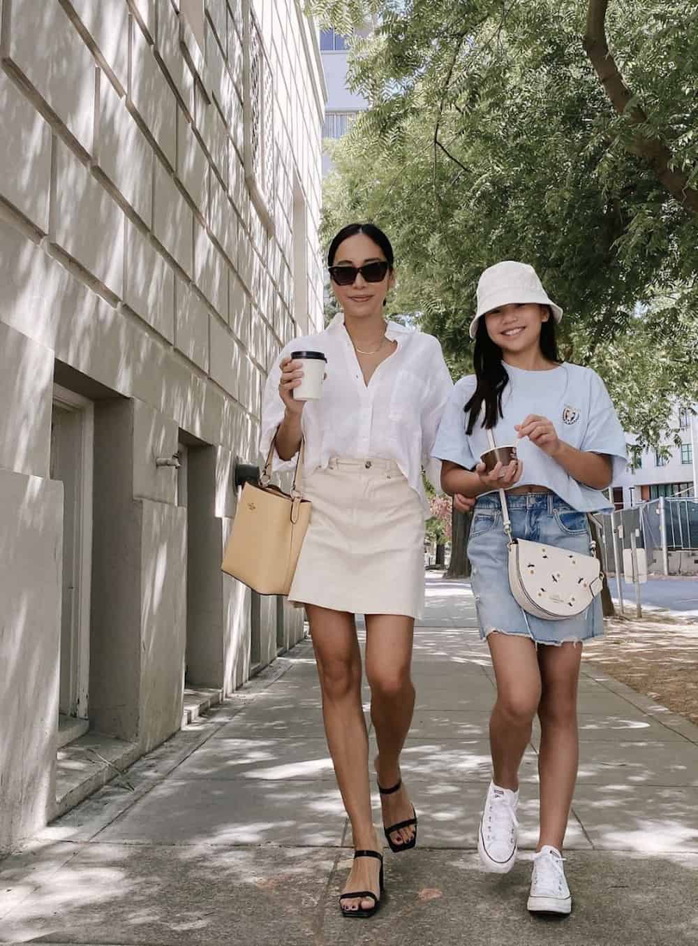 image of an asian woman walking with her daughter, she is wearing a white button up shirt, cream denim skirt, and black sandals
