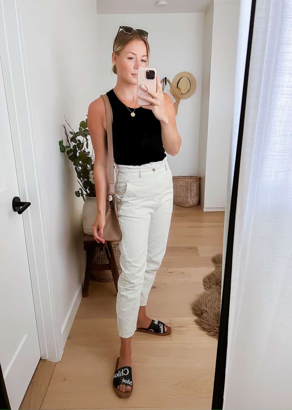 image of a woman wearing a black tank top, cream color paperbag pants and black sandals
