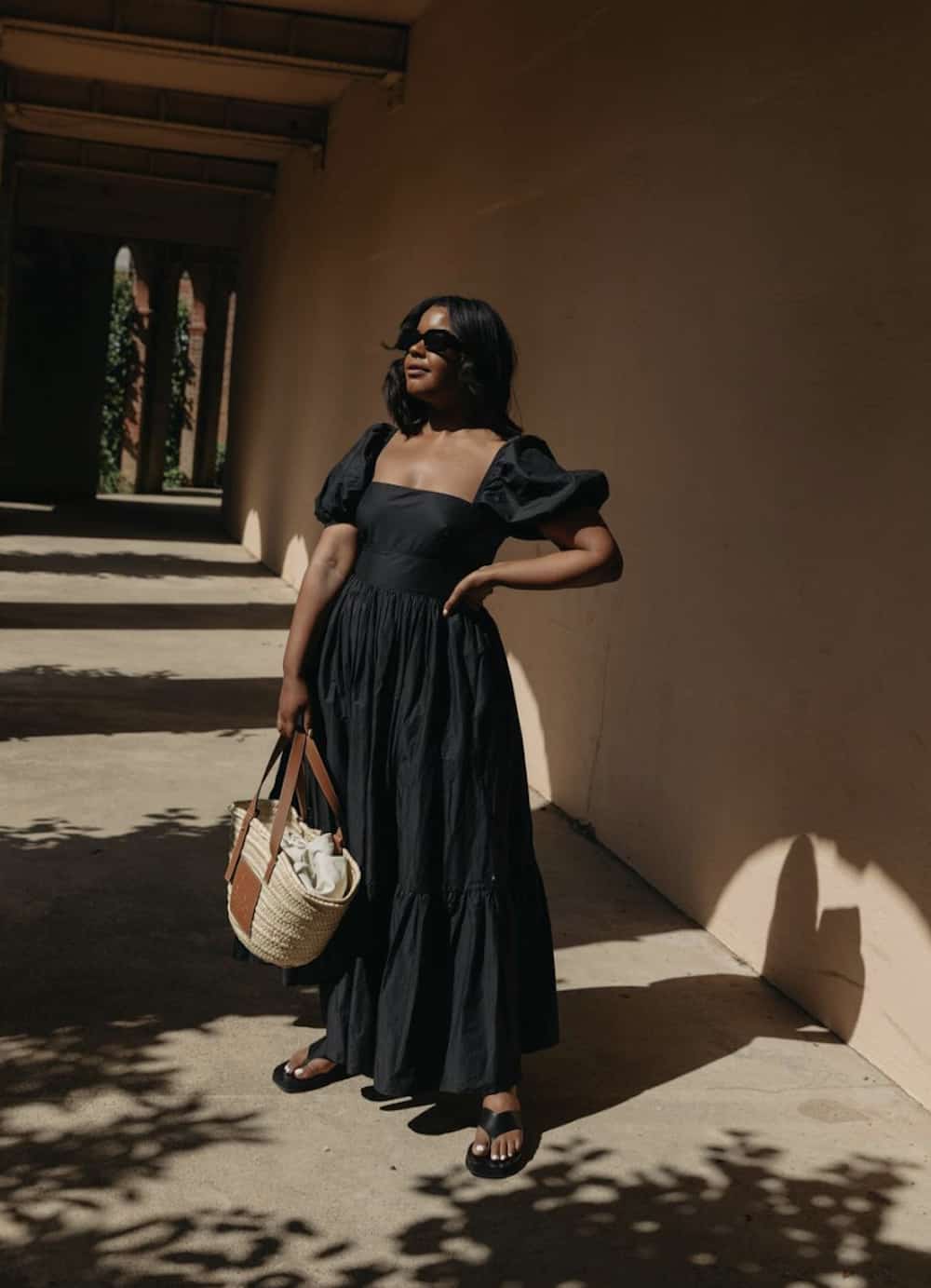 image of a black woman wearing a long black dress with black sandals and a straw tote basket bag
