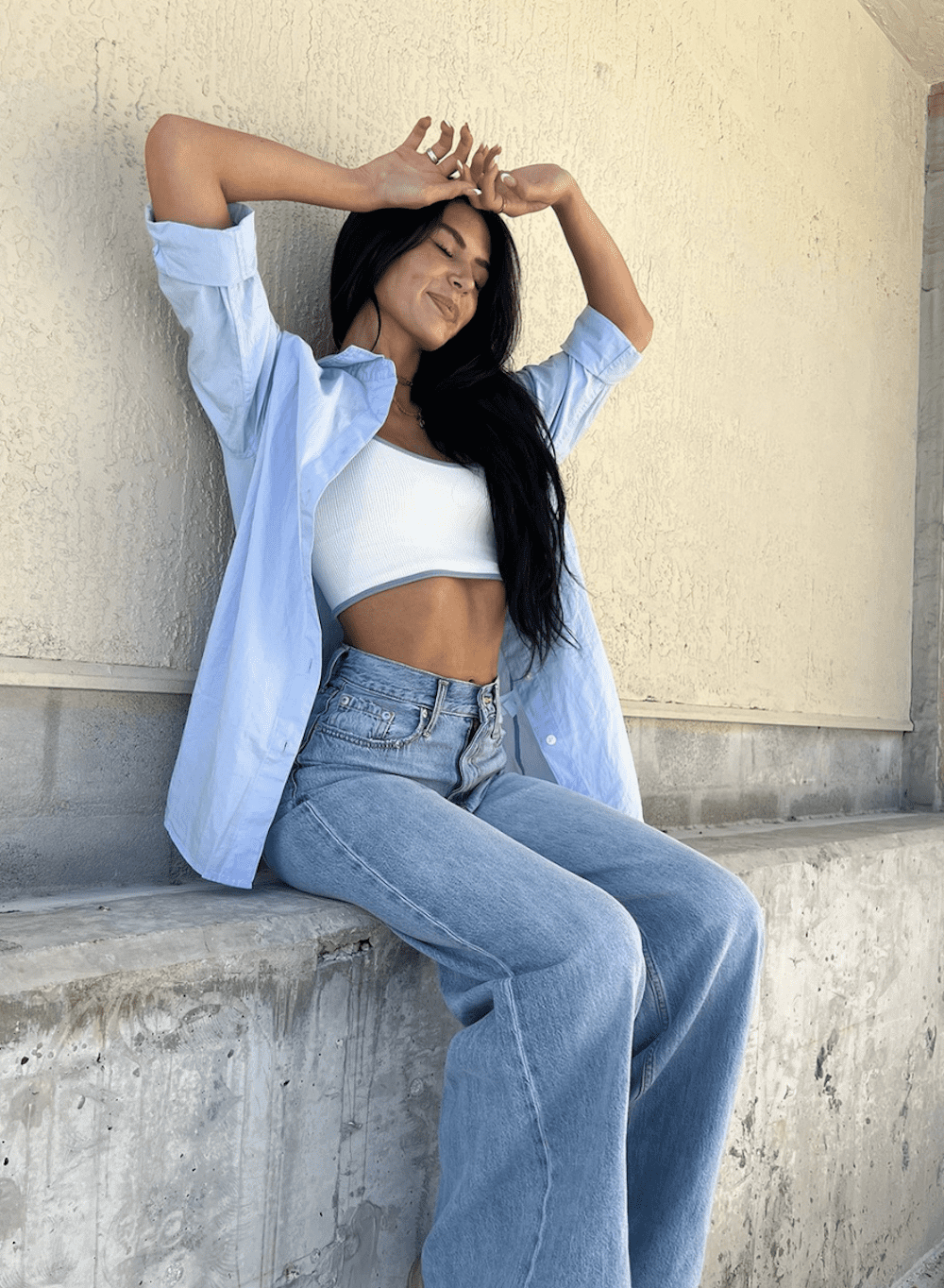 image of a young woman in a blue button up shirt with white crop top underneath and high rise blue jeans