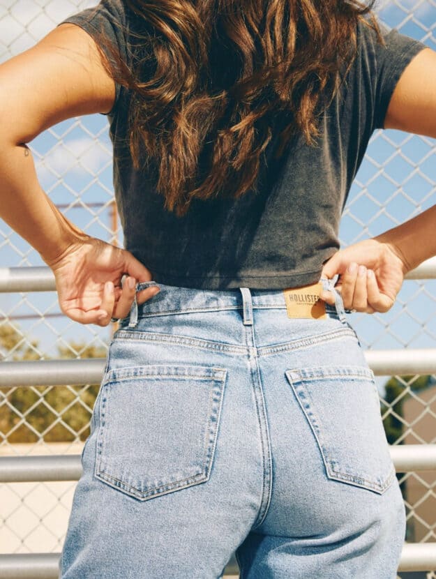 Image of a woman from the back pulling up her jeans belt loops wearing blue jeans and a black t-shirt