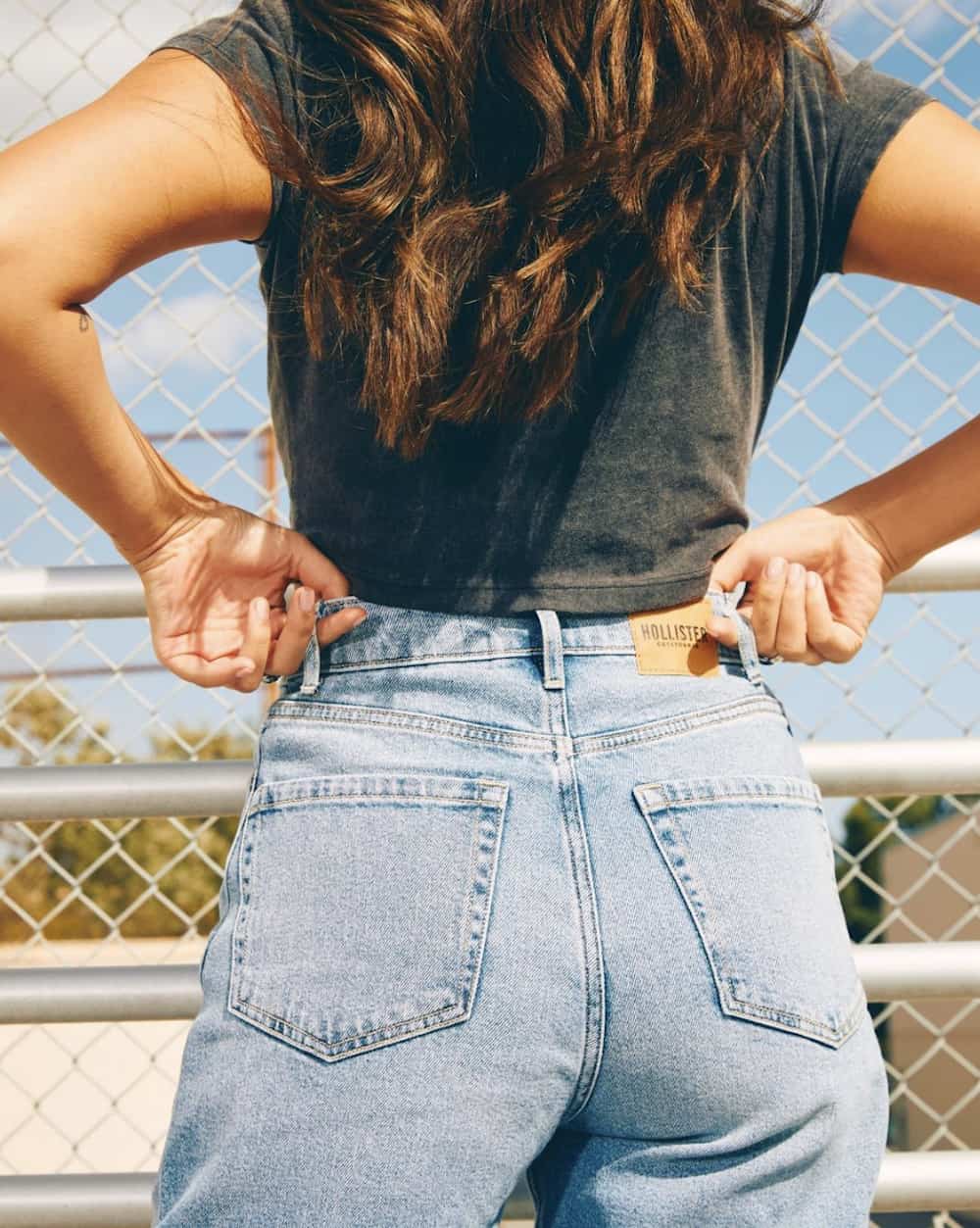 Image of a woman from the back pulling up her jeans belt loops wearing blue jeans and a black t-shirt