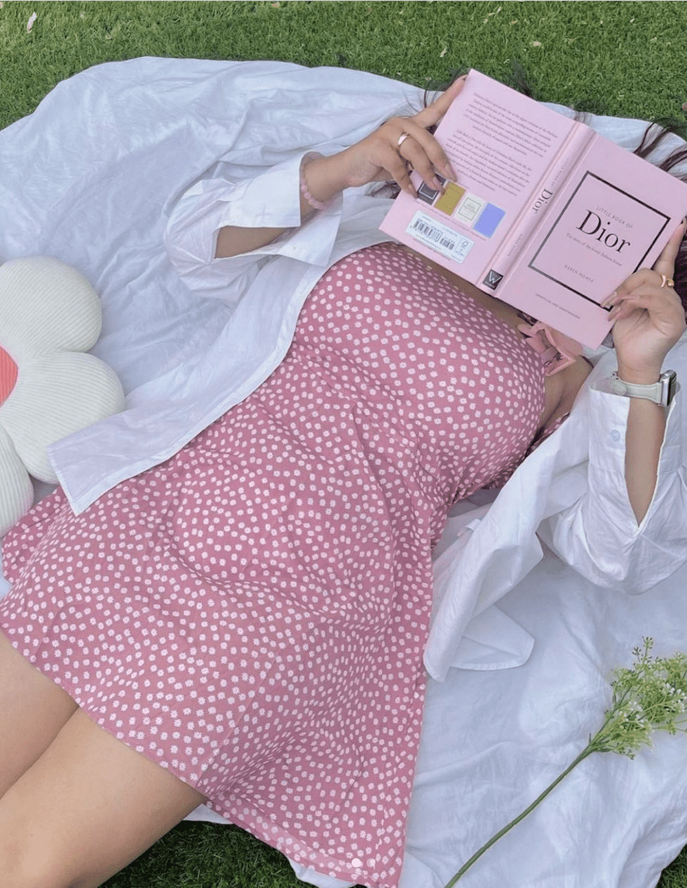 image of a woman laying on a blanket wearing a pink dress reading a pink book