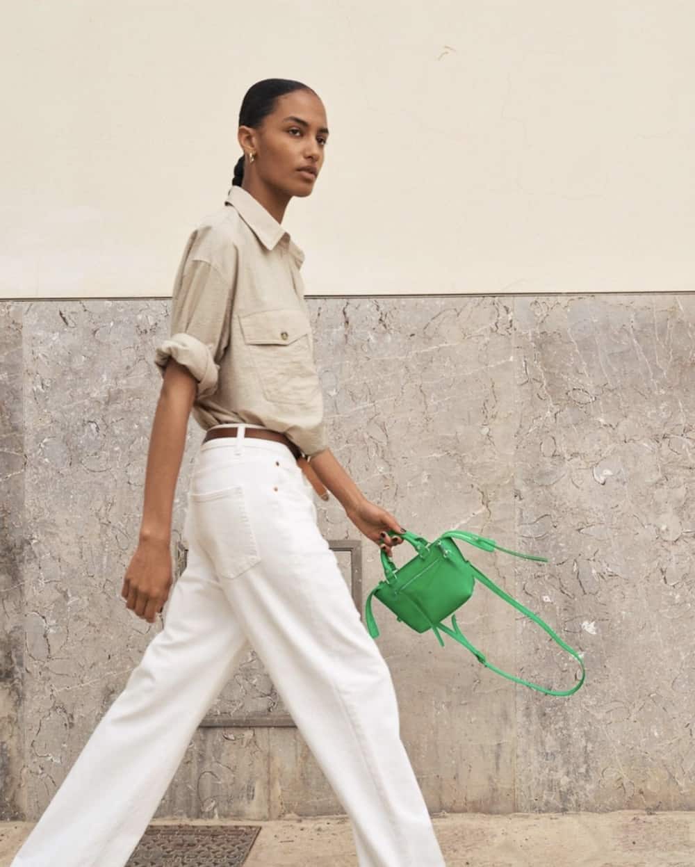 Woman wearing white and an oatmeal colored button down with a green bag.