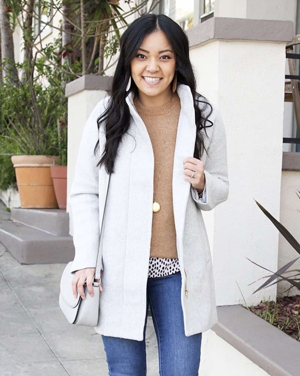 Woman wearing a white coat, brown sweater and jeans.