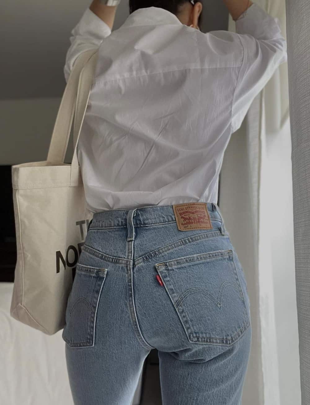 Woman wearing jeans, a white button down and a canvas bag.