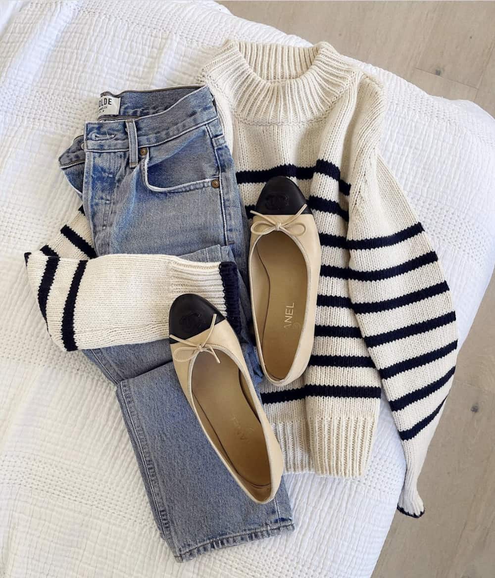 image of an outfit flatlay with a striped black and white knit sweater, jeans, and beige ballet flats with a black cap toe