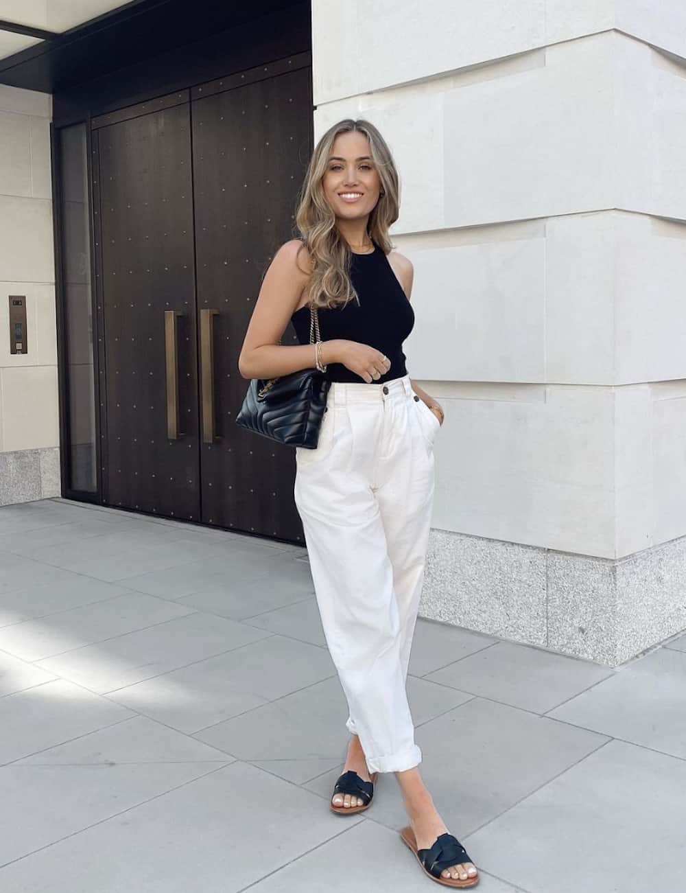 image of a woman in a cute outfit with white trousers, a black tank top, and black sandals