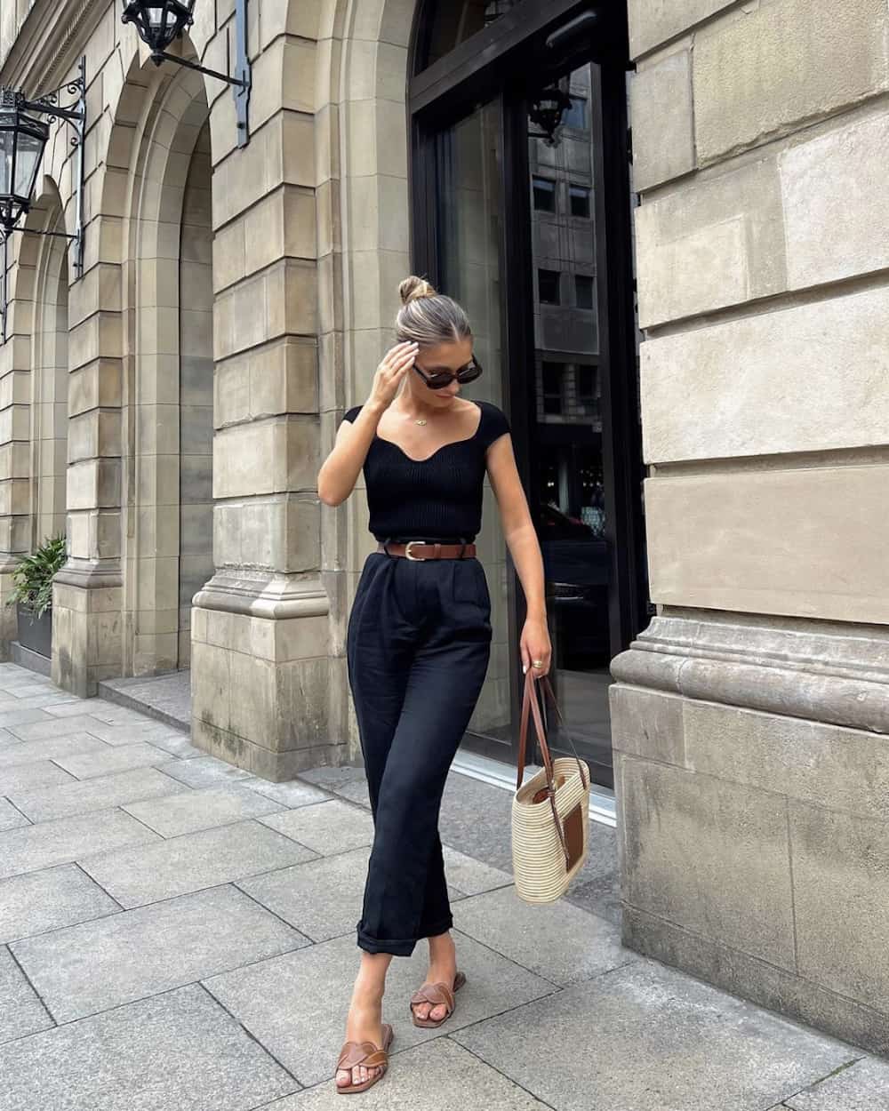 image of a woman in an all black outfit with black pants and a black ribbed knit top, brown sandals and a straw bag