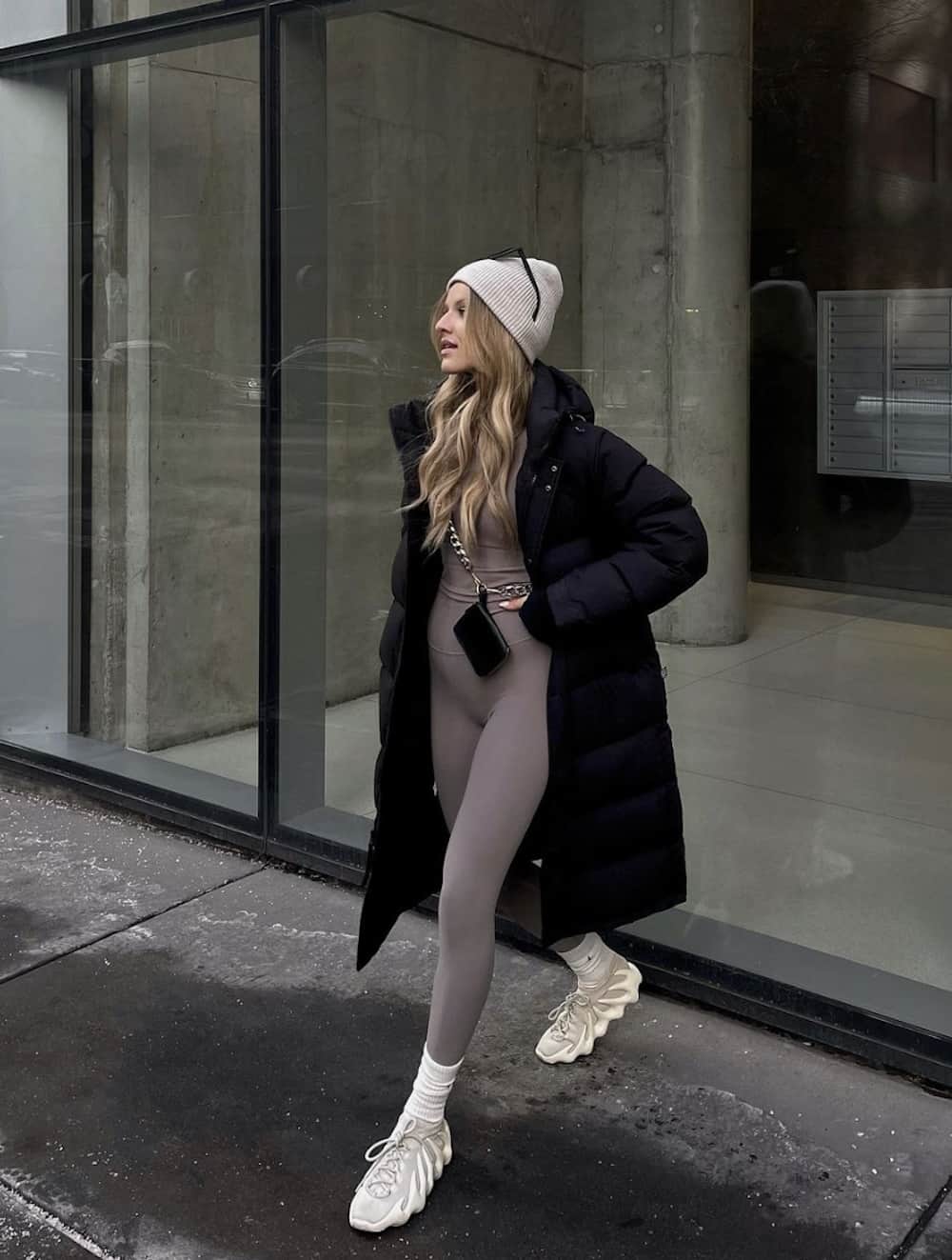 image of a woman wearing a long black puffer coat, beanie, and matching mauve leggings and crop top set with sneakers